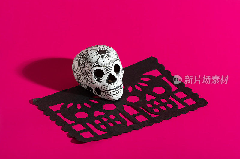 死亡的一天的陶器头骨(calavera)在黑色papel picado在热粉色背景，Dia de Muertos背景